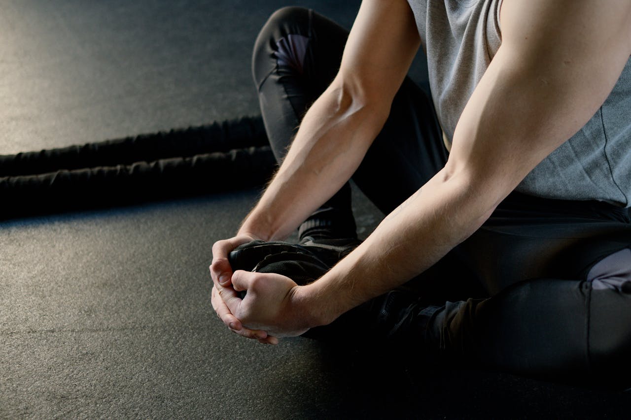 Man sitting on gym floor, stretching legs, preparing for workout routine.